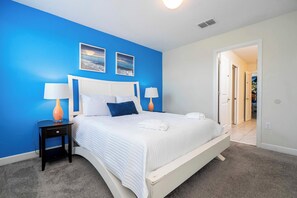 Un dormitorio con cama blanca, paredes azules y dos cuadros enmarcados.