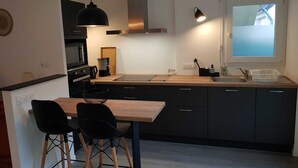 Une cuisine moderne avec un îlot central, des chaises noires, une table en bois et une fenêtre donnant sur un beau paysage.
