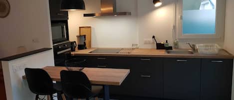 A modern kitchen with a central island, black chairs, a wooden table, and a window with a view.