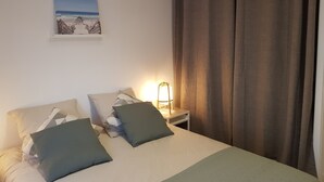 Un lit bien fait, avec des oreillers, une lampe de chevet et un tableau encadré accroché au mur.