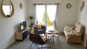 Un salon comprenant un canapé, un fauteuil, une table basse, un téléviseur et une plante en pot.