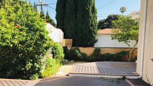 Eine Holzterrasse mit Basketballkorb, umgeben von dichtem Grün und hohen Bäumen.