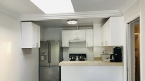Eine kompakte Küche mit weißen Schränken, einem Edelstahl-Kühlschrank, einer Kaffeemaschine und einem Oberlicht.