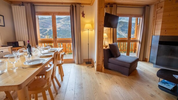 A wooden interior with a dining table set for six, a sofa, a TV, and a fireplace.