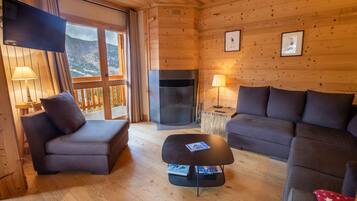 A cozy cabin interior with a fireplace, two sofas, a coffee table, and a TV mounted on the wall.