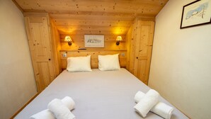 A wooden cabin room with a bed, two wall-mounted lamps, and a framed picture on the wall.