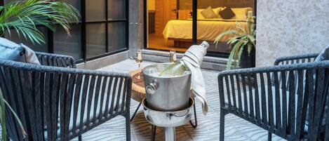 An outdoor seating area with two wicker chairs, a table with a metal container, and a glass of wine.