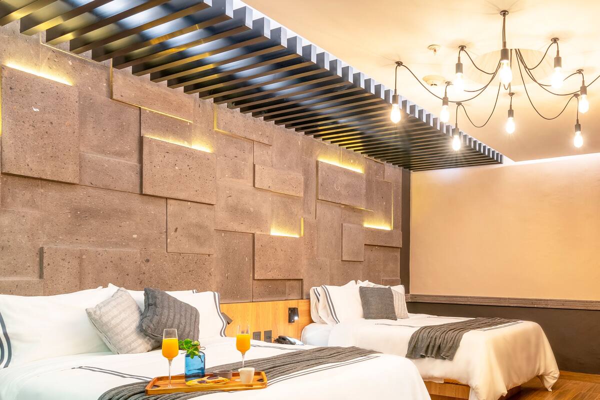 A modern hotel room with two beds, a wooden floor, a stone wall, and a ceiling light fixture.