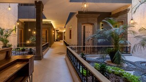 A hotel corridor with a wooden bench, potted plants, and a stone fountain. - Hotel Patio Santiago (Querétaro)
