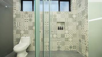 A bathroom with a patterned tile wall, a toilet, and a glass shower enclosure.
