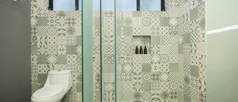 Un baño con pared de azulejos estampados, un inodoro y una cabina de ducha de vidrio.