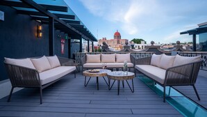 An outdoor seating area with two sofas and two round tables, a glass water feature, and a view of a historic building with a red dome. - Hotel Patio Santiago (Querétaro)