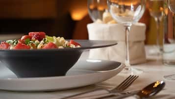 A dining table with a bowl of salad, a plate, a glass of wine, and cutlery.