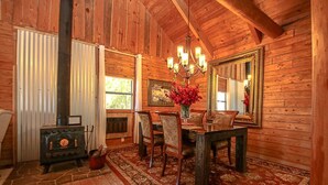 Un intérieur rustique en bois, avec une table à manger, des chaises, un lustre et un grand miroir.