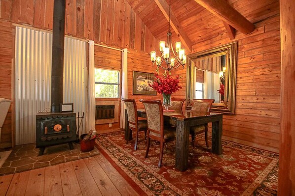 A rustic wooden interior with a dining table, chairs, a chandelier, and a large mirror.
