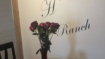 Uma mesa de jantar com um vaso de rosas vermelhas, uma garrafa e um pote. A parede ao fundo tem o texto "Flyin' H Ranch".