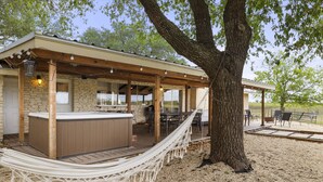 A covered outdoor area with a hot tub, seating, and a hammock. - San Marcos Farm Stay — Mini Cows, Hot Tub & Games — Sleeps 12 (San Marcos)
