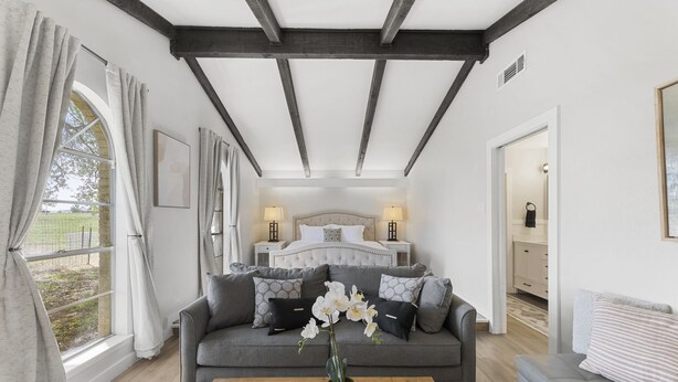 A bedroom with a large bed, a sofa, a coffee table with flowers, and a view of the outdoors. - San Marcos Farm Stay — Mini Cows, Hot Tub & Games — Sleeps 12 (San Marcos)
