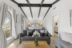 A bedroom with a large bed, a sofa, a coffee table with flowers, and a view of the outdoors.