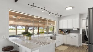 A modern kitchen with white cabinetry, a large island with a marble countertop, a built-in oven, and a refrigerator. - San Marcos Farm Stay — Mini Cows, Hot Tub & Games — Sleeps 12 (San Marcos)