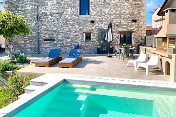 A stone building with a swimming pool, lounge chairs, and outdoor seating.