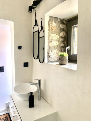 A bathroom with a white sink, black towel holder, and a stone wall. - The Backyard (Eva)