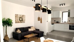 A modern living room with a black sofa, a coffee table, and a dining area with a white table and woven placemats. - The Backyard (Eva)