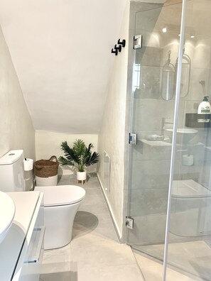 A modern bathroom with a glass shower enclosure, a toilet, a sink, and a potted plant.