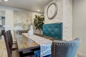 Un coin repas avec une table en bois, une tête de lit recouverte d’un tissu bleu et une horloge murale.
