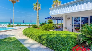 A resort with a pool, palm trees, and a building with a covered patio. - Gorgeous Beachside Condo in superior Longboat Location (Longboat Key)