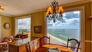 A dining area with a view of the ocean, a chandelier, and a wooden table. - Gorgeous Beachside Condo in superior Longboat Location (Longboat Key)