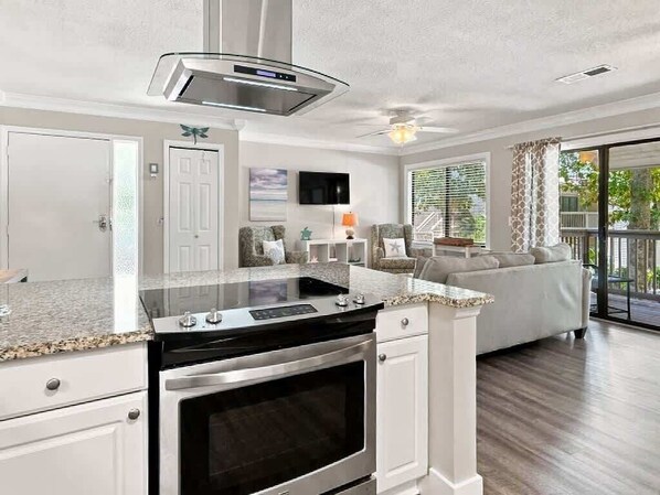 A modern kitchen with a built-in stove, oven, and microwave, a dining area with a table and chairs, and a living room with a sofa and a TV.