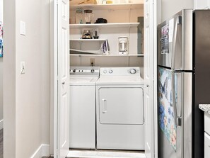 Une cuisine compacte équipée d’un lave-linge et d’un sèche-linge intégrés, d’un réfrigérateur et d’une étagère pour ranger les ustensiles de cuisine.