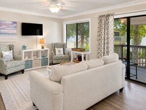 A living room with a sofa, armchairs, a TV, a ceiling fan, and a window with blinds.