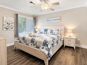 A bedroom with a bed, bedside tables, a ceiling fan, and artwork on the walls.