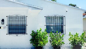 Un edificio blanco con una puerta negra y dos ventanas con barrotes de metal.