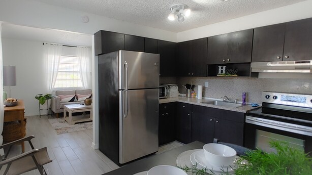 Una cocina compacta con armarios oscuros, un refrigerador de acero inoxidable, un microondas y una estufa.