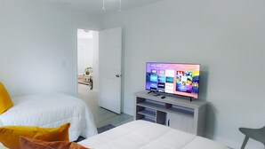 Una habitación de hotel con una cama, un televisor mostrando servicios de streaming y una puerta que da a otra habitación.