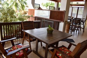 A wooden table and chairs with floral cushions, a potted plant, and a view of greenery outside.