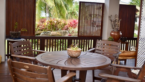 A wooden deck with a round table and chairs, surrounded by a wooden fence and tropical plants. - Aito 2 in Muri (Muri)