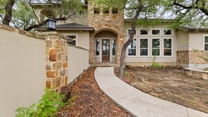Una casa de piedra con una entrada central en arco, un patio cubierto y un camino de piedra que conduce a la entrada.