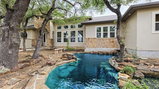 Una piscina con agua cristalina, rodeada de construcciones de piedra y ladrillo, y árboles.