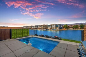A swimming pool with lounge chairs, a small kiddie pool, and a wooden fence.