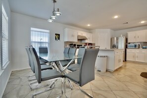 Une cuisine moderne avec des meubles blancs, des appareils en acier inoxydable et une table à manger en verre, assortie de chaises.