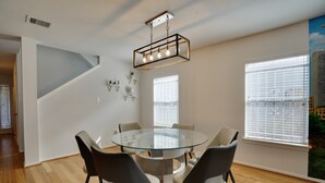 A modern dining area with a glass table surrounded by chairs, a geometric ceiling light fixture, and large windows with blinds. - Houston Wall Mural,  A Getaway Escape  (Houston)