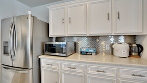 A kitchen with white cabinetry, a stainless steel refrigerator, a microwave, a slow cooker, and a coffee maker. - Houston Wall Mural,  A Getaway Escape  (Houston)