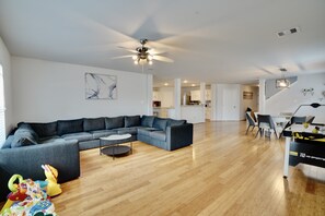 Un vaste espace de vie comprenant un canapé d’angle, une table basse ronde et un ventilateur de plafond.