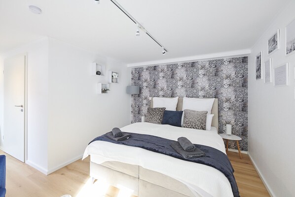 A modern bedroom with a bed, bedside tables, a wall-mounted lamp, and a patterned wallpaper.