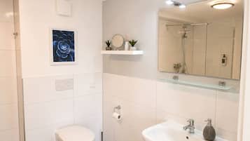 Ein modernes Badezimmer mit Toilette, Waschbecken, Spiegel und Dusche.