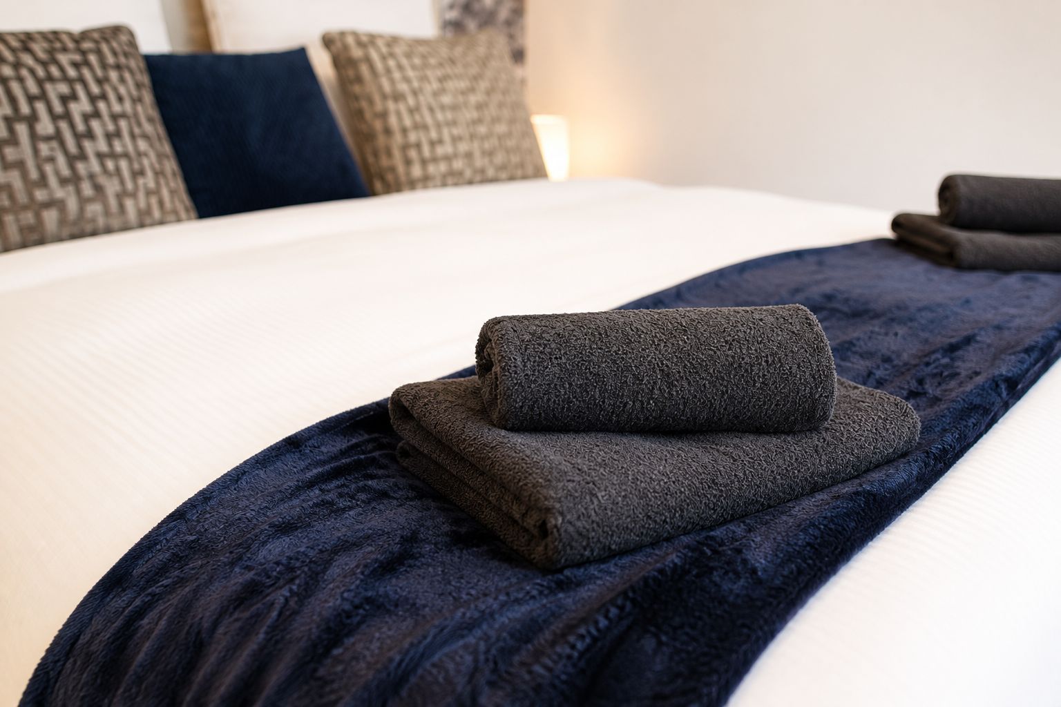 A neatly made bed with a dark blue blanket and a folded towel.